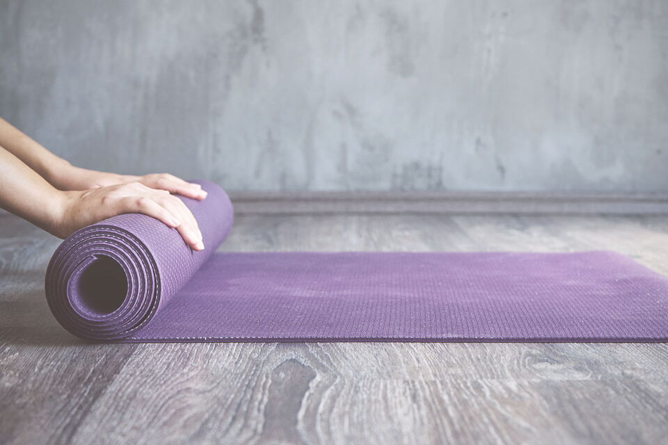 Nahaufnahme von Händen, die eine lila Yogamatte ausrollen