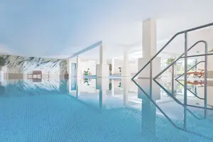 Blick über das gesamte Becken hinweg durch das Schwimmbad. Im Vordergrund die Treppe ins Wasser, im Hintergrund Wandmalereien.